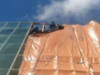 Colaboradores da SELF Engenharia em acesso por cordas removendo vidros da fachada e colocando lona de cobertura